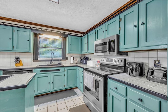 kitchen with a textured ceiling, backsplash, appliances with stainless steel finishes, sink, and light tile patterned flooring