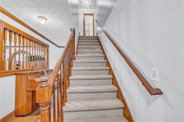 staircase featuring ornamental molding, a textured ceiling, and hardwood / wood-style floors