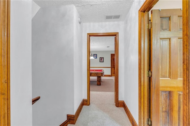 hallway with light carpet and a textured ceiling