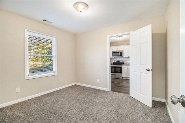 unfurnished room with visible vents, baseboards, and dark colored carpet