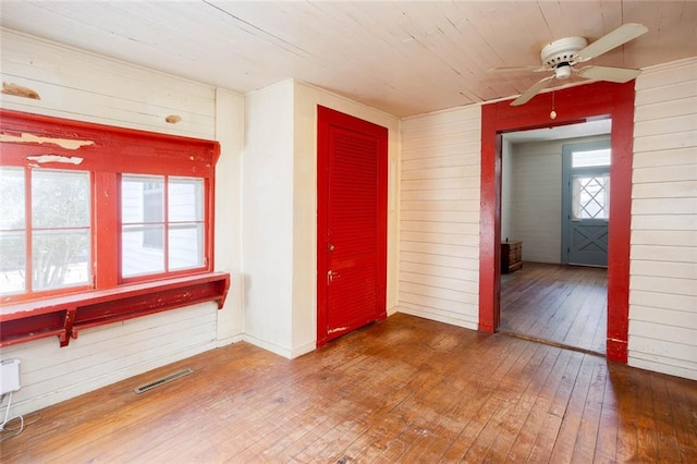 unfurnished room with wood-type flooring, ceiling fan, and wood walls