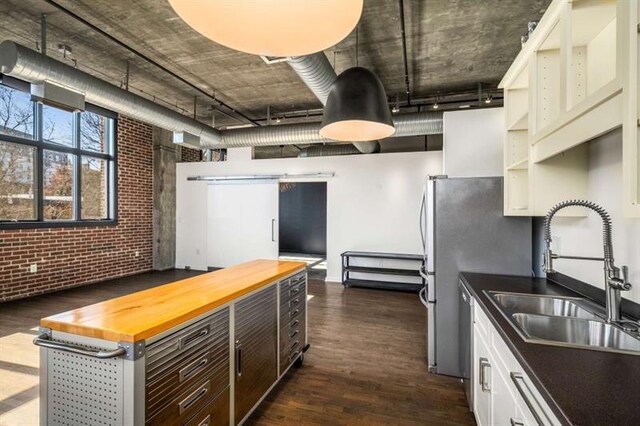 kitchen featuring dark wood-style floors, white cabinetry, a sink, brick wall, and butcher block countertops