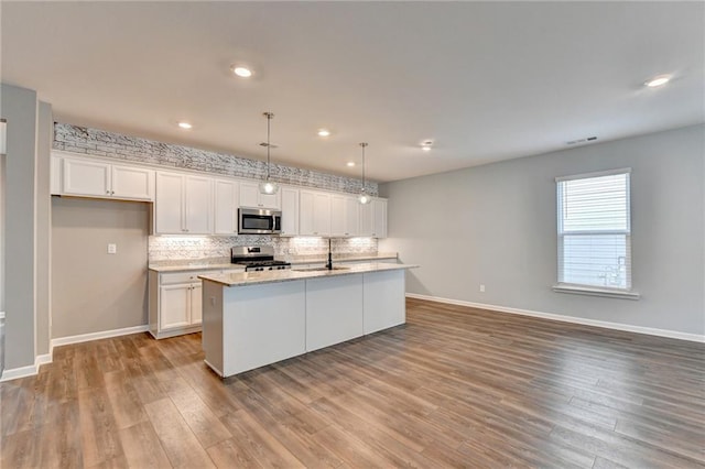 kitchen with hanging light fixtures, a kitchen island with sink, stainless steel appliances, and white cabinets