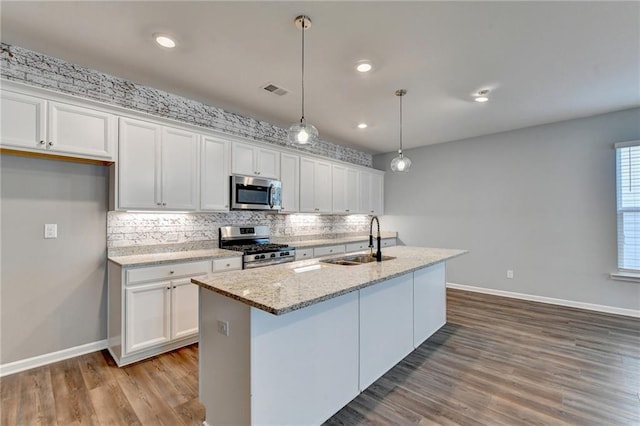 kitchen with stainless steel appliances, white cabinets, sink, hanging light fixtures, and a center island with sink