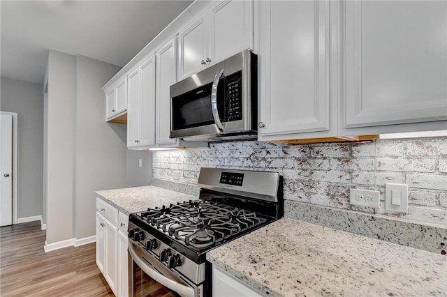 kitchen with light stone counters, tasteful backsplash, light hardwood / wood-style flooring, white cabinetry, and appliances with stainless steel finishes