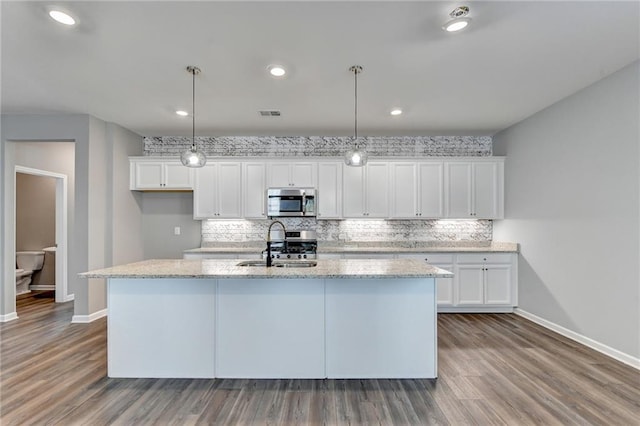 kitchen with hardwood / wood-style floors, decorative light fixtures, a center island with sink, sink, and white cabinetry