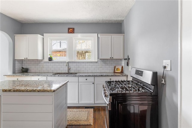 kitchen with light stone counters, white cabinetry, stainless steel range with gas cooktop, and sink