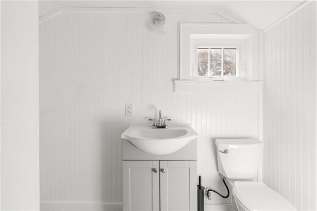 bathroom with wood walls, vanity, lofted ceiling, and toilet