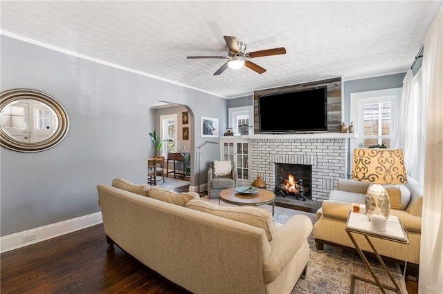 living room with crown molding, dark hardwood / wood-style floors, ceiling fan, a textured ceiling, and a fireplace