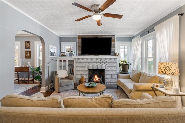 living room featuring a textured ceiling, ceiling fan, crown molding, wood-type flooring, and a fireplace