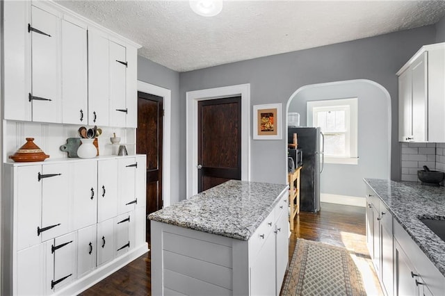 kitchen featuring white cabinets, dark hardwood / wood-style flooring, backsplash, and light stone counters