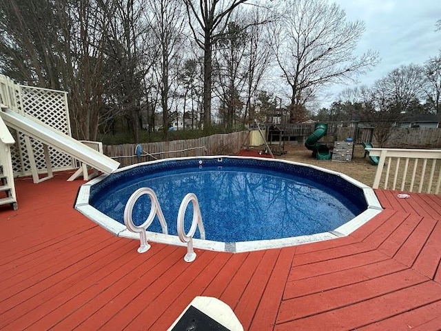 view of pool with a playground and a wooden deck