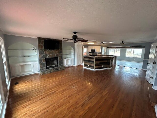 unfurnished living room with a textured ceiling, ceiling fan, crown molding, hardwood / wood-style flooring, and a stone fireplace