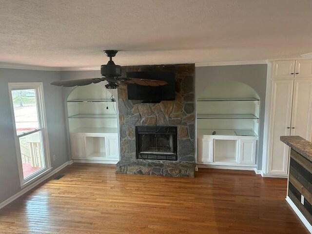 unfurnished living room with crown molding, hardwood / wood-style flooring, ceiling fan, a fireplace, and a textured ceiling