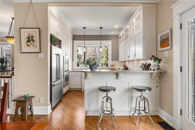 kitchen featuring pendant lighting, stainless steel appliances, light stone counters, ornamental molding, and white cabinets