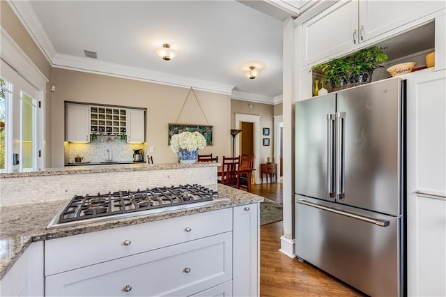 kitchen with white cabinetry, crown molding, stainless steel appliances, light stone countertops, and backsplash