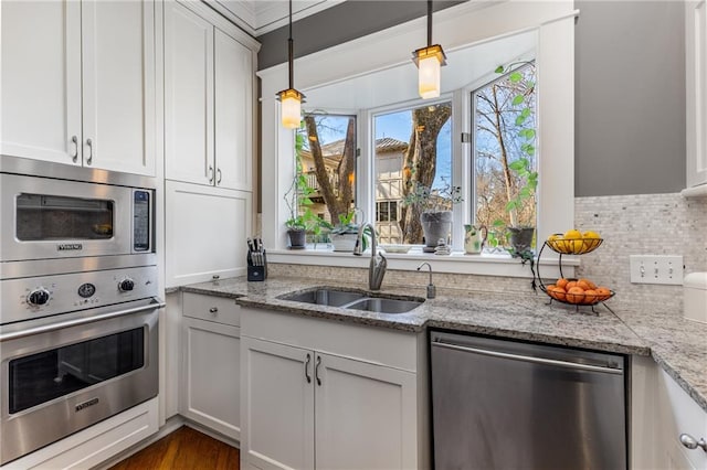 kitchen with appliances with stainless steel finishes, white cabinetry, sink, hanging light fixtures, and light stone countertops