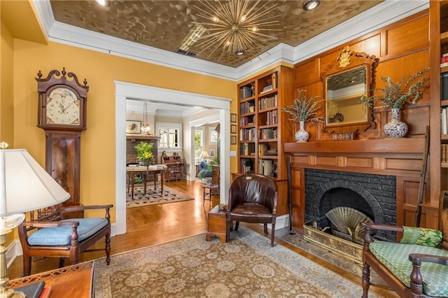 living area featuring an inviting chandelier, built in features, a fireplace, ornamental molding, and light wood-type flooring