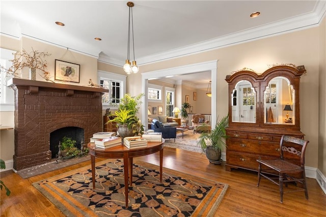 sitting room with ornamental molding, wood-type flooring, and a brick fireplace