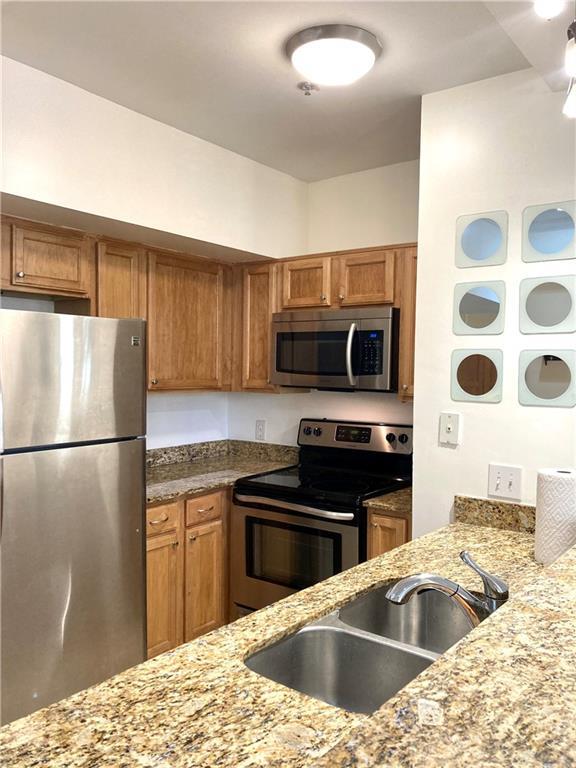 kitchen featuring a sink, brown cabinets, appliances with stainless steel finishes, and light stone countertops