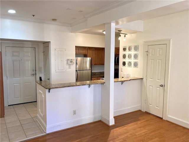 kitchen with brown cabinetry, a peninsula, freestanding refrigerator, and crown molding