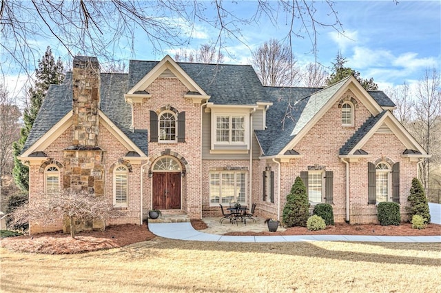 view of front of house with a shingled roof, a front lawn, a chimney, and brick siding