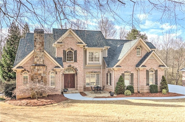 view of front of property with roof with shingles, a chimney, a front lawn, and brick siding