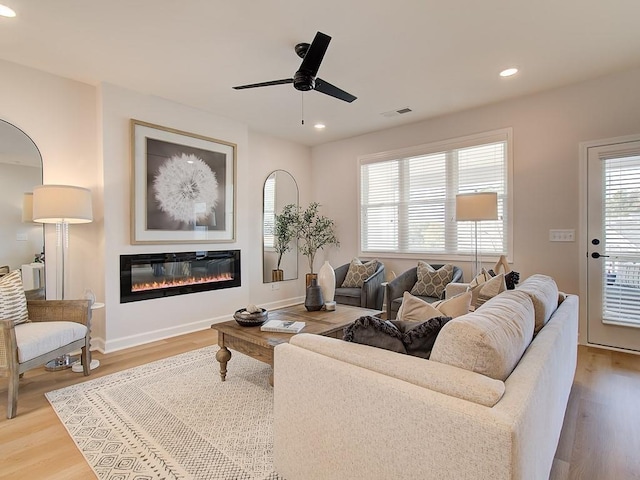 living area with visible vents, wood finished floors, a glass covered fireplace, recessed lighting, and ceiling fan