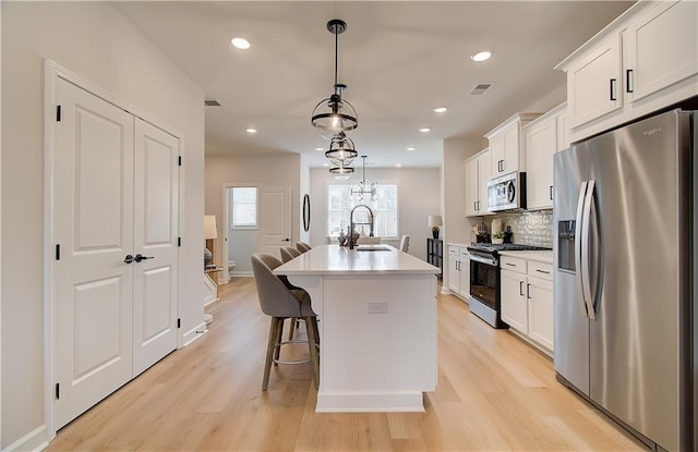 kitchen with visible vents, a center island with sink, a sink, stainless steel appliances, and white cabinets