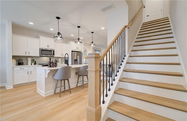 kitchen featuring a breakfast bar area, visible vents, appliances with stainless steel finishes, white cabinetry, and light wood-type flooring