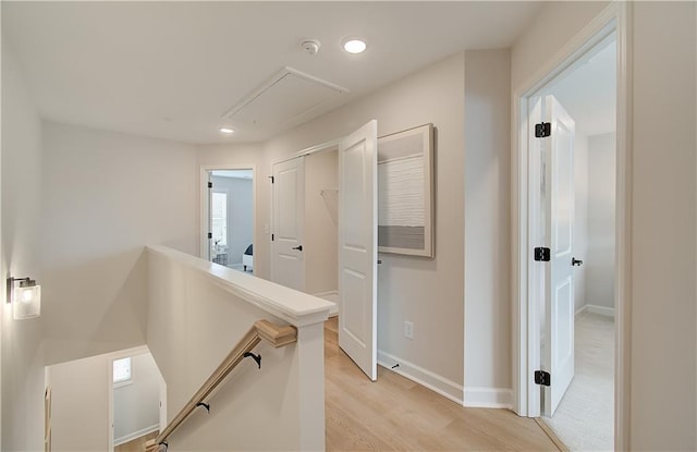 hall with an upstairs landing, recessed lighting, light wood-style floors, baseboards, and attic access