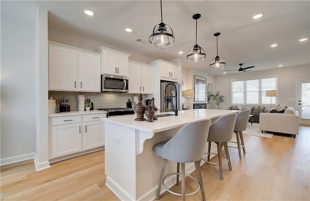 kitchen with a breakfast bar, a kitchen island with sink, a sink, white cabinets, and appliances with stainless steel finishes