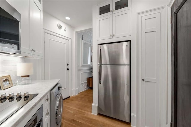 75 Ponce De Leon Ave NE Unit 1006, Atlanta, GA 30308 - kitchen featuring appliances with stainless steel finishes, washer / dryer, white cabinetry, light wood finished floors, and glass insert cabinets