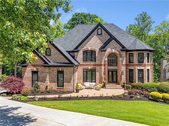 french country home featuring brick siding, a front lawn, and roof with shingles