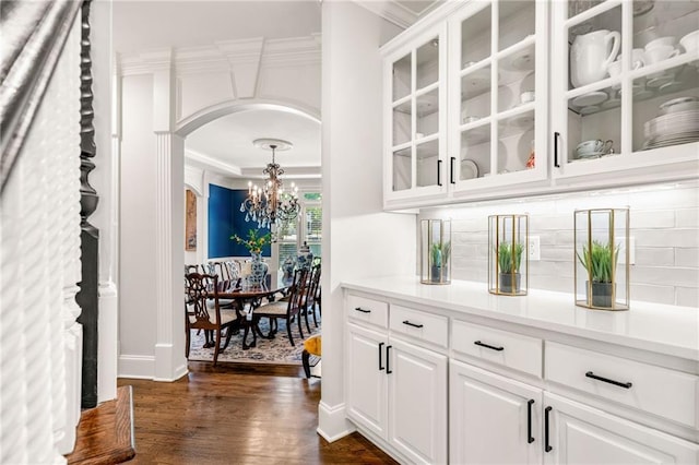 bar with arched walkways, a chandelier, decorative backsplash, ornamental molding, and dark wood-style floors