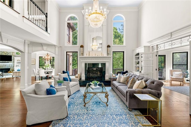 living area featuring a fireplace with raised hearth, a chandelier, healthy amount of natural light, wood finished floors, and a high ceiling
