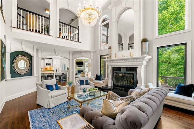 living room featuring a premium fireplace, a towering ceiling, a chandelier, wood finished floors, and baseboards