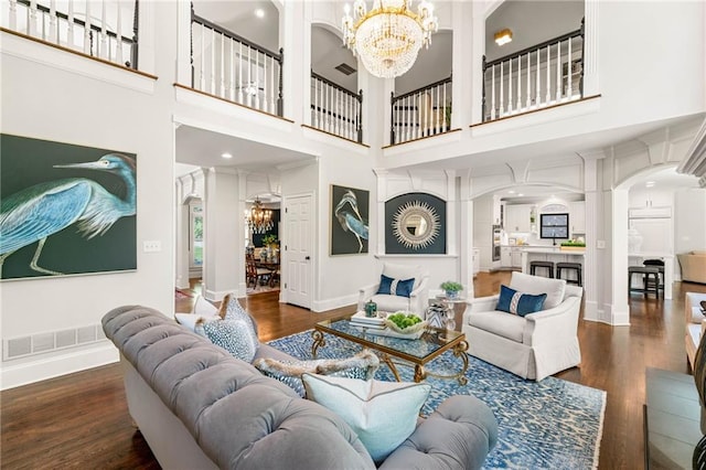 living room featuring a chandelier, arched walkways, wood finished floors, a high ceiling, and baseboards