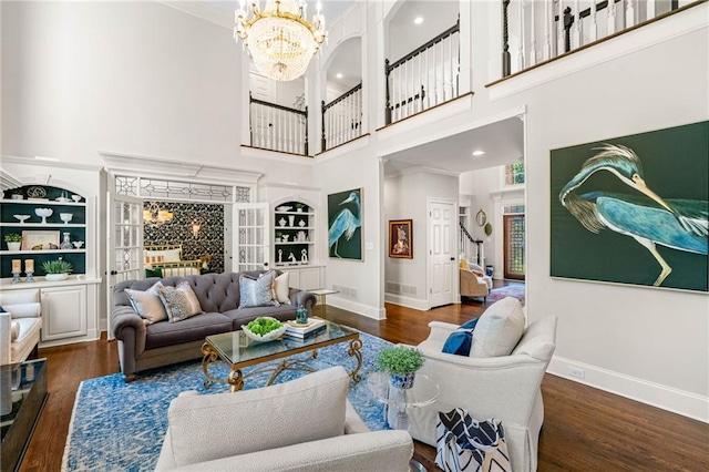 living area with a chandelier, built in features, wood finished floors, baseboards, and a high ceiling