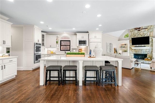 kitchen featuring appliances with stainless steel finishes, a kitchen breakfast bar, a stone fireplace, dark wood finished floors, and recessed lighting