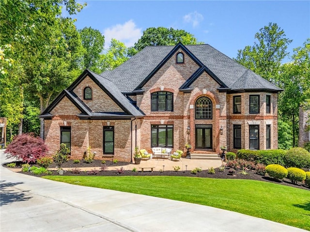 french country inspired facade with a front yard, brick siding, and roof with shingles