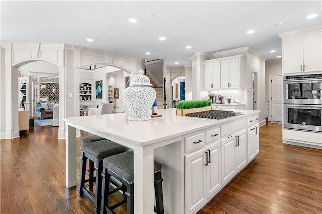 kitchen featuring arched walkways, stainless steel appliances, a center island, white cabinets, and dark wood-style floors