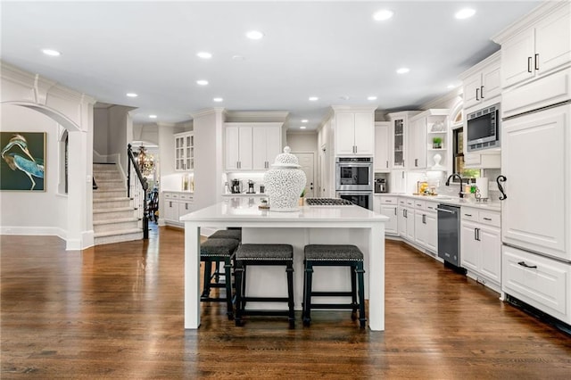 kitchen featuring appliances with stainless steel finishes, a kitchen bar, white cabinets, a center island, and glass insert cabinets