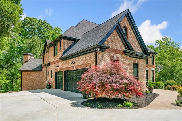 view of side of property with roof with shingles, concrete driveway, brick siding, and a chimney