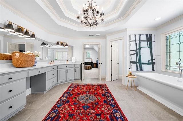 full bathroom featuring a chandelier, ornamental molding, a freestanding bath, a raised ceiling, and vanity