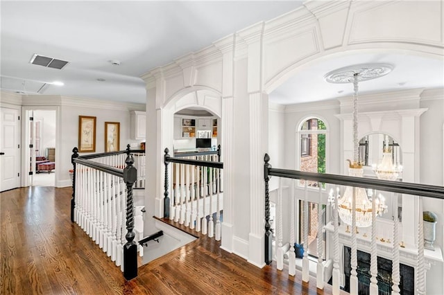 hall with an upstairs landing, dark wood finished floors, crown molding, a chandelier, and arched walkways