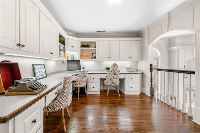office with built in desk, dark wood-type flooring, and arched walkways