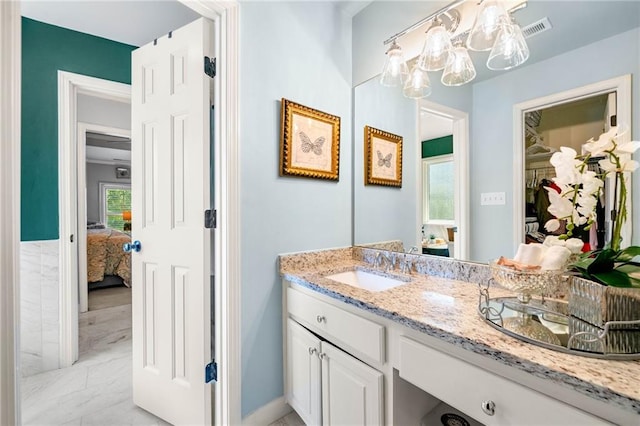 ensuite bathroom with marble finish flooring, vanity, a chandelier, a spacious closet, and baseboards