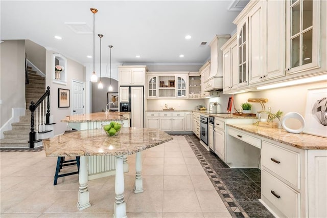 kitchen with paneled built in refrigerator, oven, a kitchen bar, a center island with sink, and light stone counters