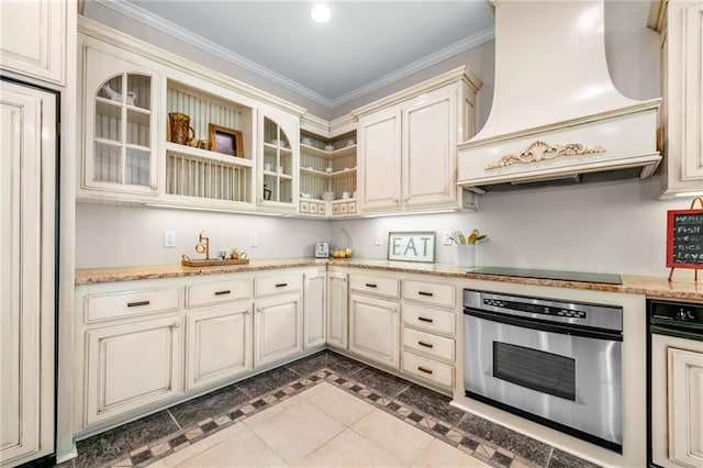 kitchen with stainless steel oven, cream cabinetry, premium range hood, crown molding, and open shelves